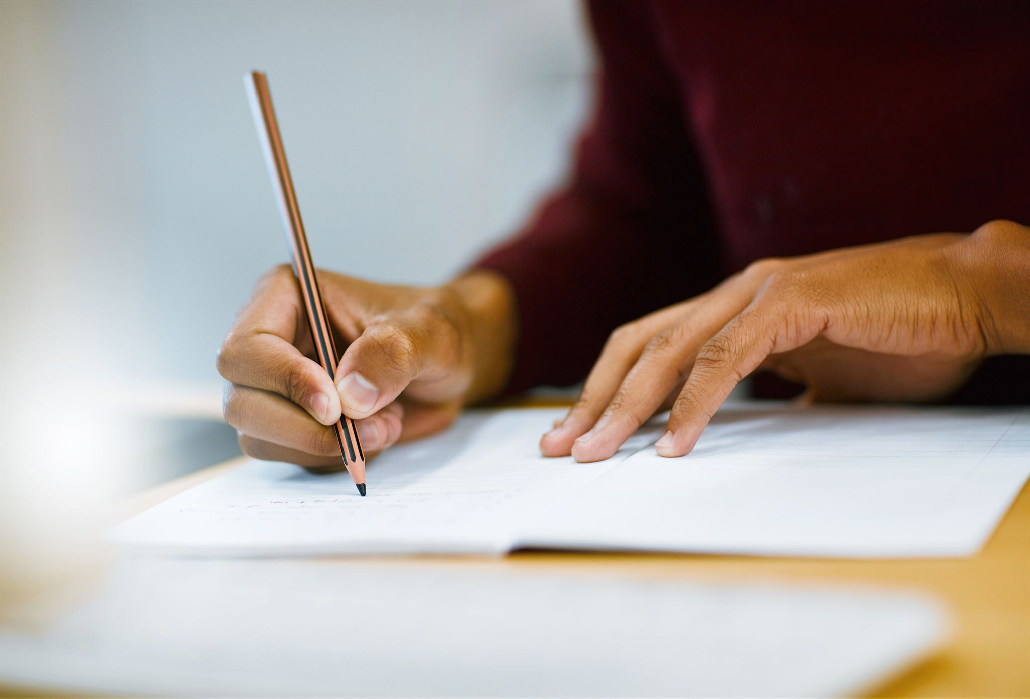 Seated-person-at-wood-table,-holding-pencil-and-writing-on-lined-paper-page-in-open-notebook